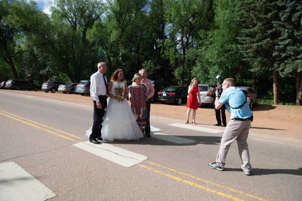 A photographer is taking a picture of a bride and her family in the road.