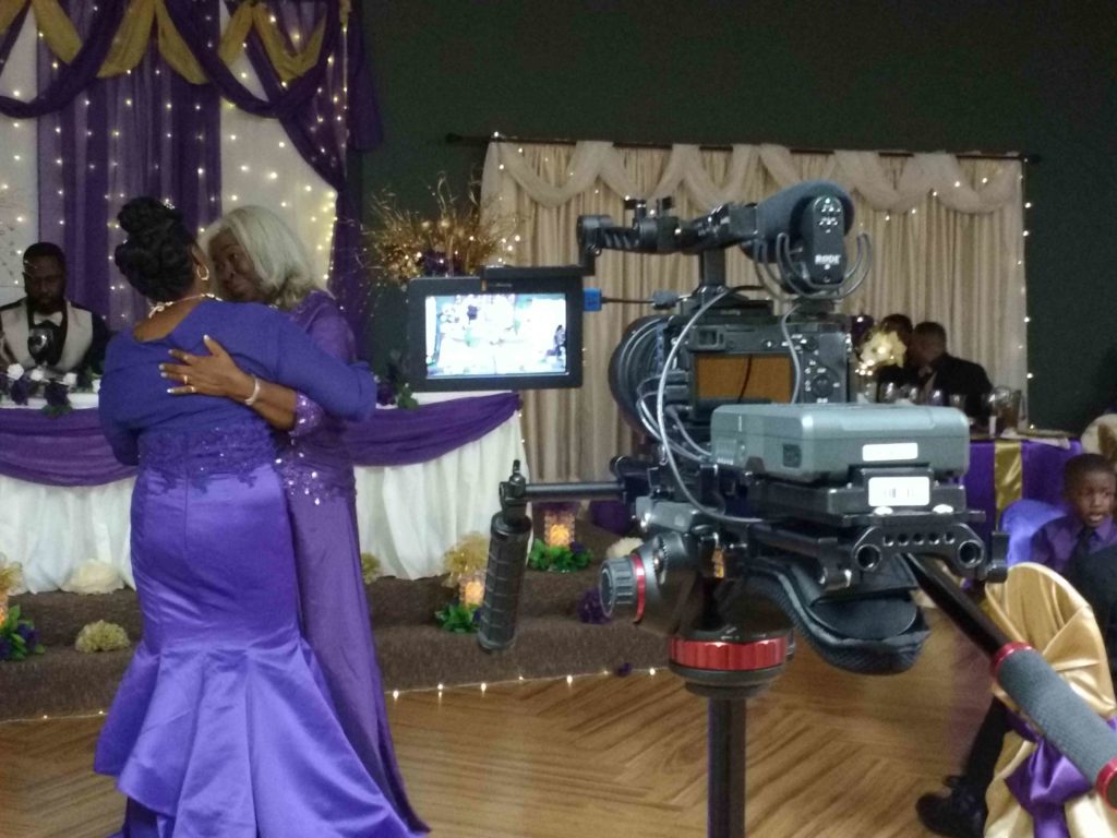 A dance at a wedding. Two women are dancing together on the left of the frame, while a camera is recording them on the right.